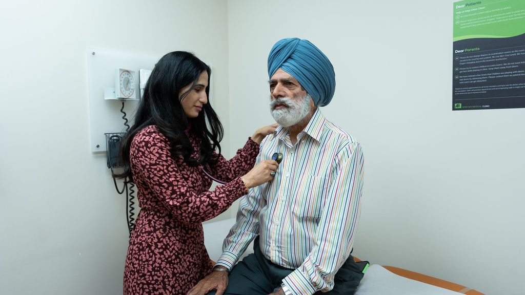 A physician listens to an older patient's chest with a stethoscope in a clinic examination room.